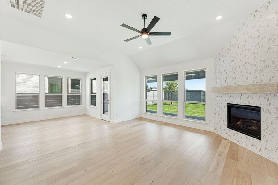 Open living room with light hardwood floors, tiled fireplace, ceiling fan, and large windows overlooking backyard Open living room with light hardwood floors, tiled fireplace, ceiling fan, and large windows overlooking backyard