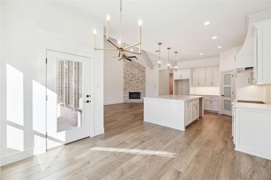 Kitchen with pendant lighting, a center island with sink, white cabinets, vaulted ceiling, and decorative backsplash