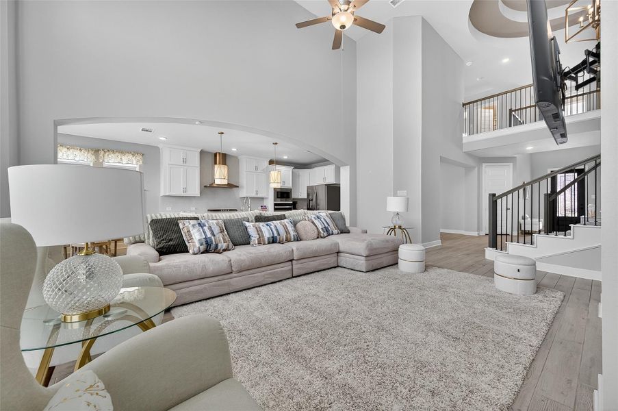 This inviting living room boasts a double-height ceiling, statement lighting, and a beautifully tiled fireplace. A curved staircase and open archways add architectural charm and flow.