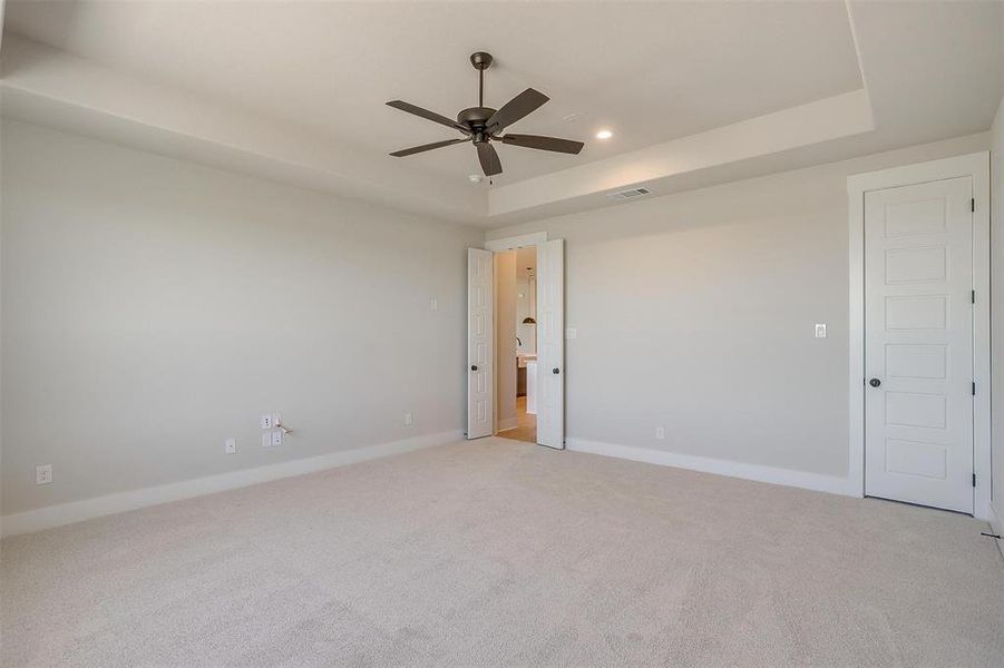 Empty room with baseboards, recessed lighting, a ceiling fan, a raised ceiling, and light colored carpet Empty room with baseboards, recessed lighting, a ceiling fan, a raised ceiling, and light colored carpet