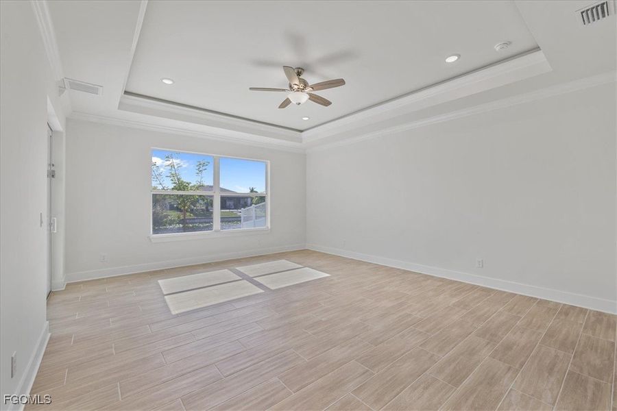 Empty room featuring ornamental molding, a raised ceiling, a ceiling fan, wood finish floors, and recessed lighting