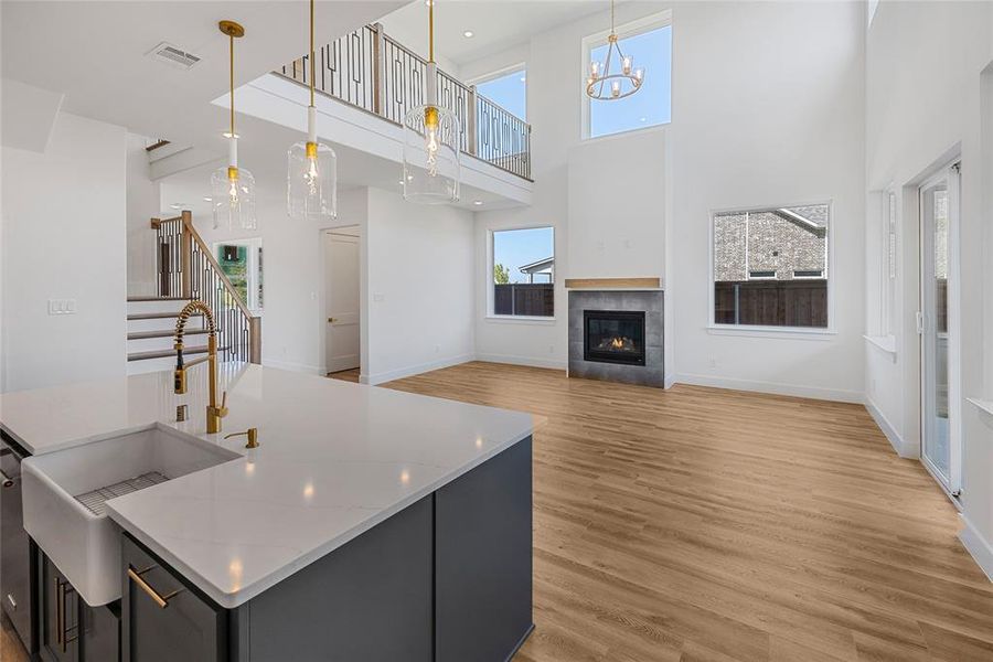 Kitchen with a high ceiling, a tiled fireplace, decorative light fixtures, and light hardwood / wood-style floors