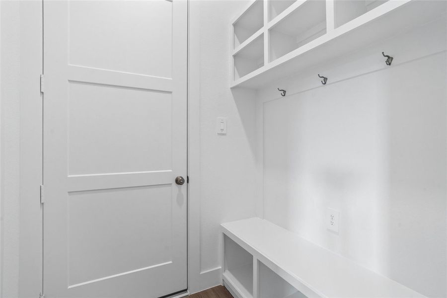 Step into this highly functional and stylish mudroom drop zone, an essential feature for a busy household. The space boasts custom-built white cabinetry and shelving, providing generous storage for coats, bags, and shoes. A comfortable built-in bench offers a convenient spot to sit, while three sleek hooks keep outerwear tidy and accessible.