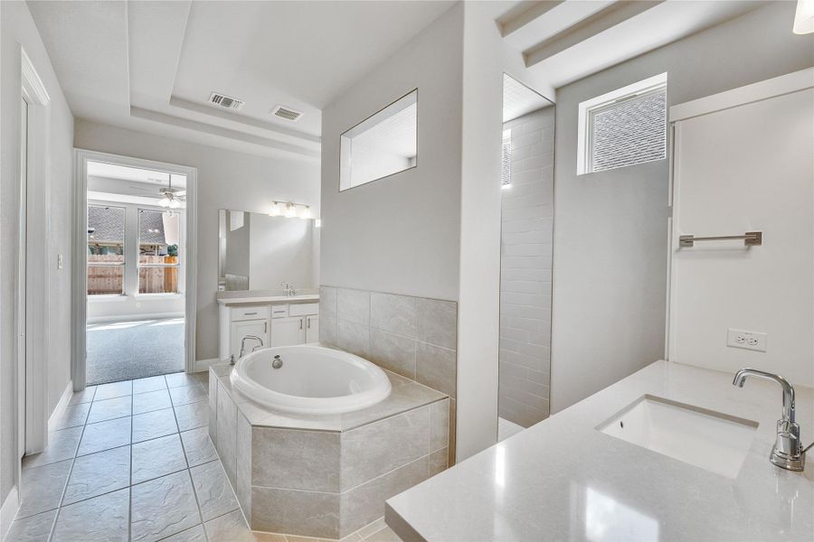 Full bath with two vanities, a garden tub, a ceiling fan, light tile patterned floors, and a tray ceiling Full bath with two vanities, a garden tub, a ceiling fan, light tile patterned floors, and a tray ceiling