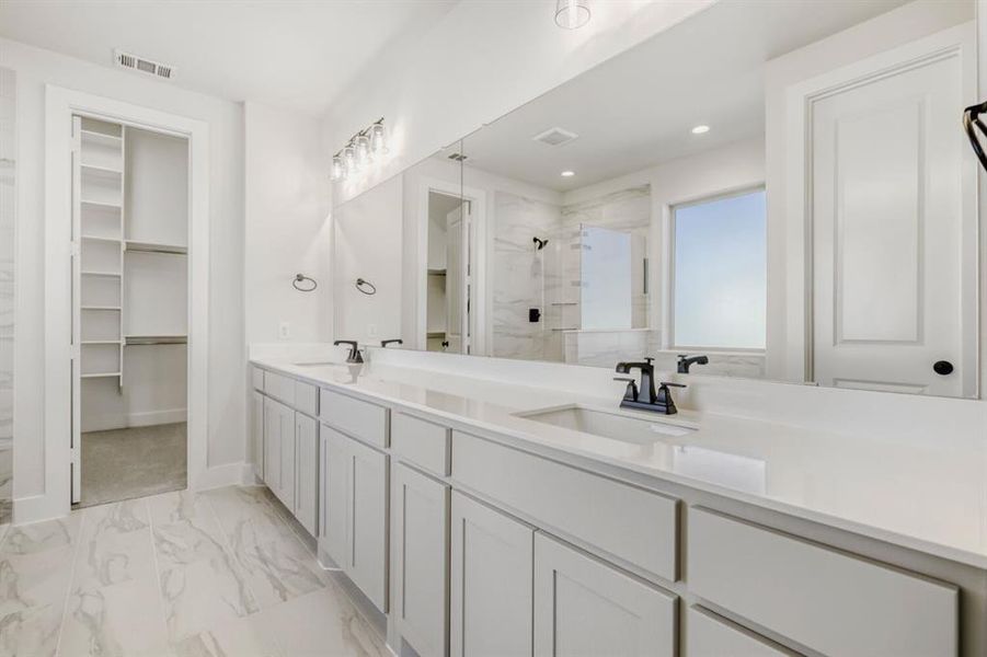 Bathroom with a marble finish shower, double vanity, a walk in closet, light marble finish floors, and recessed lighting
