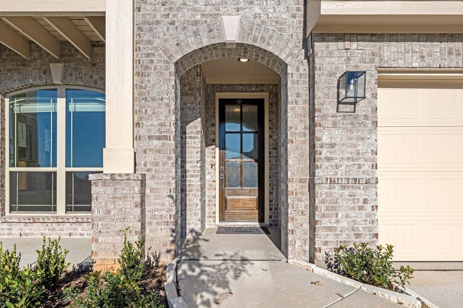 Brick home entrance with arched doorway, black glass front door, and wall lantern beside garage Brick home entrance with arched doorway, black glass front door, and wall lantern beside garage