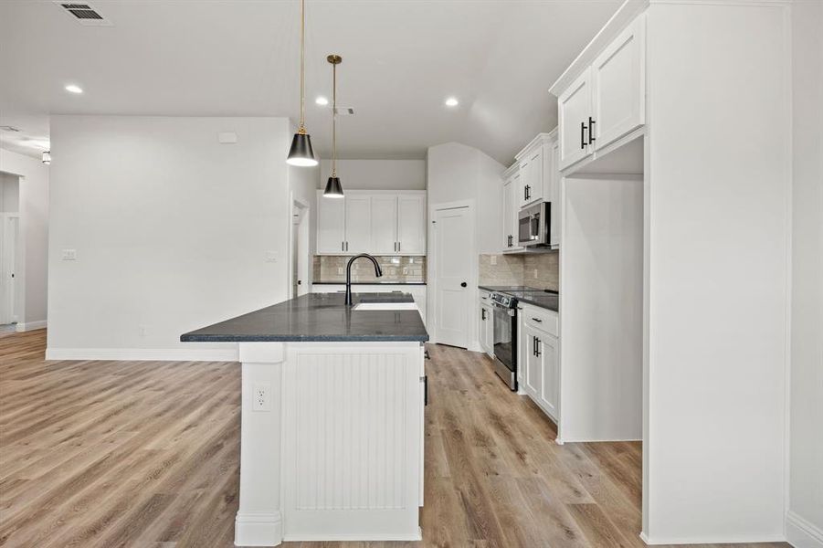 Kitchen with appliances with stainless steel finishes, white cabinetry, hanging light fixtures, a kitchen island with sink, and decorative backsplash