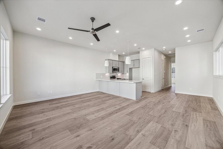 This expansive great room seamlessly blends the living and dining spaces, highlighted by beautiful wide-plank flooring and a contemporary ceiling fan that anchors the airy atmosphere.