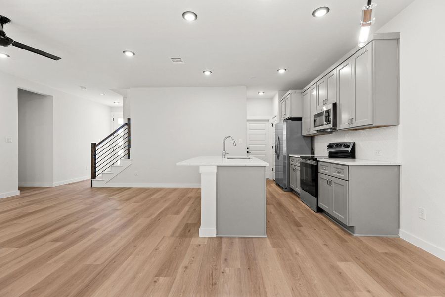 A contemporary open-concept space features light wood flooring, an island kitchen, and a staircase with sleek railings. A contemporary open-concept space features light wood flooring, an island kitchen, and a staircase with sleek railings.