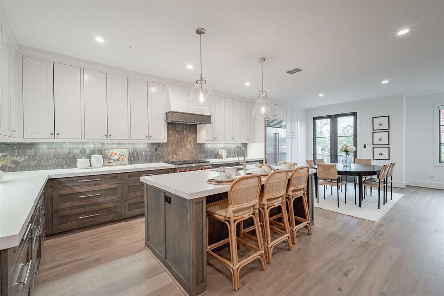 Kitchen featuring pendant lighting, white cabinets, a kitchen island with sink, stainless steel appliances, and light wood-type flooring