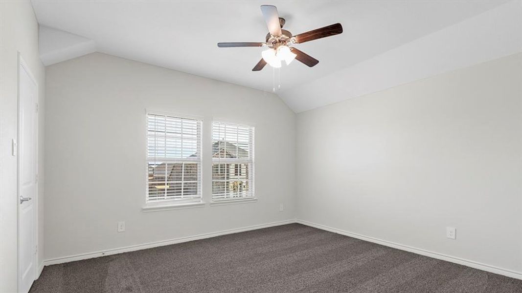 Vaulted ceiling bedroom featuring plush gray carpeting, two windows with blinds, a ceiling fan with light fixture, and white painted walls