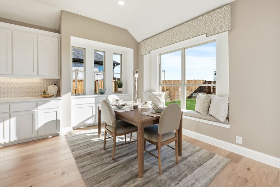 Breakfast nook with wood dining table, window seat, and hardwood floors next to white kitchen cabinets