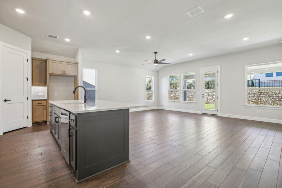 Kitchen with recessed lighting, a kitchen island with sink, backsplash, dark wood finished floors, and light stone counters Kitchen with recessed lighting, a kitchen island with sink, backsplash, dark wood finished floors, and light stone counters