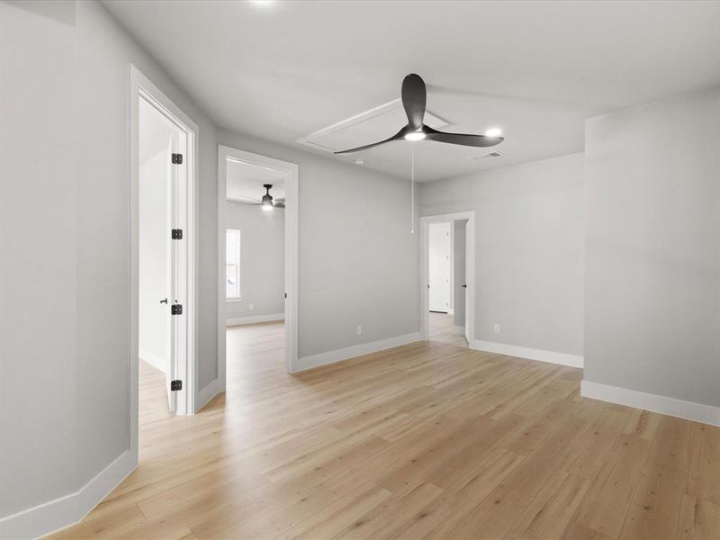 Spacious room featuring light wood-finish flooring, a modern black ceiling fan, white baseboards, and multiple doorways with black hardware Spacious room featuring light wood-finish flooring, a modern black ceiling fan, white baseboards, and multiple doorways with black hardware