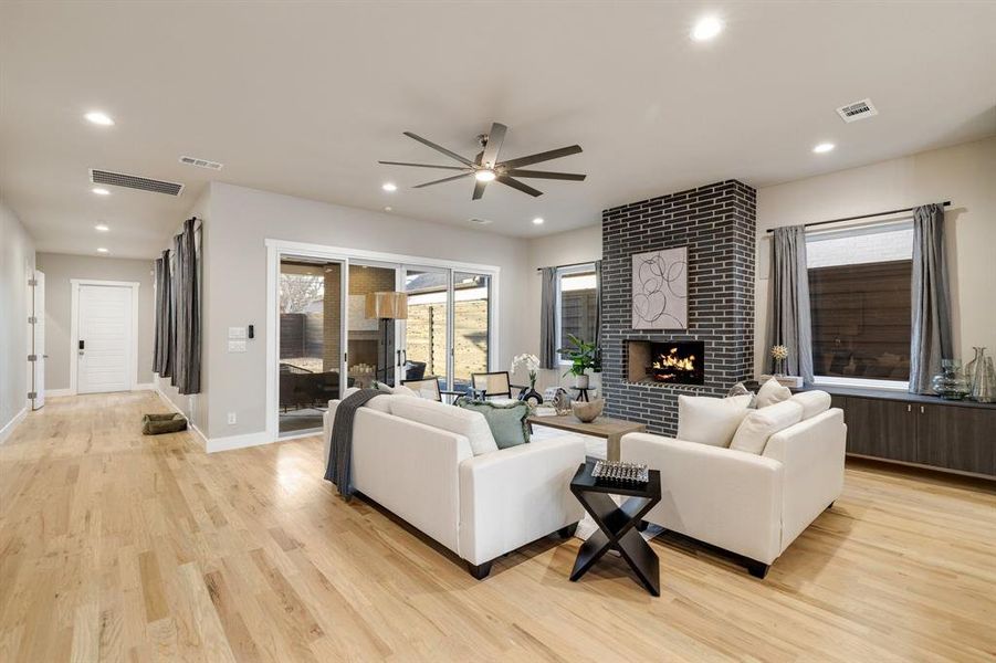 Living room with a fireplace, ceiling fan, and light hardwood / wood-style flooring