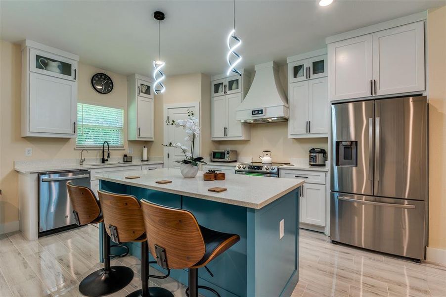 Kitchen with white full length cabinets, custom exhaust hood, stainless steel appliances, center island and pendant lighting. Kitchen with white full length cabinets, custom exhaust hood, stainless steel appliances, center island and pendant lighting.