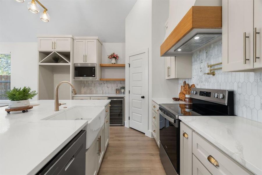 Kitchen featuring appliances with stainless steel finishes, light stone countertops, beverage cooler, light wood-style flooring, and open shelves Kitchen featuring appliances with stainless steel finishes, light stone countertops, beverage cooler, light wood-style flooring, and open shelves