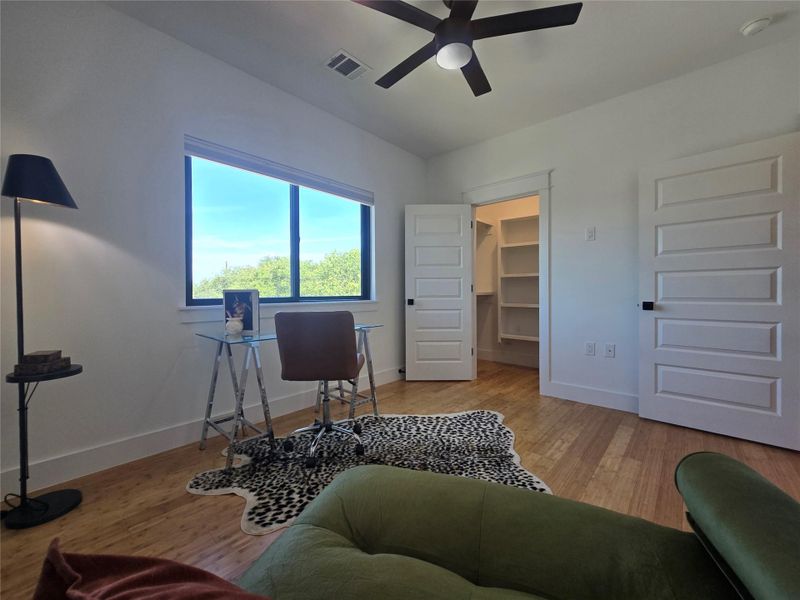 Warm wood flooring and clean white walls frame a quiet work space with natural light.