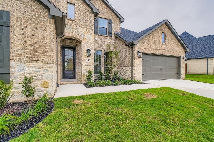 French country inspired facade featuring brick siding, a front lawn, concrete driveway, and stone siding French country inspired facade featuring brick siding, a front lawn, concrete driveway, and stone siding