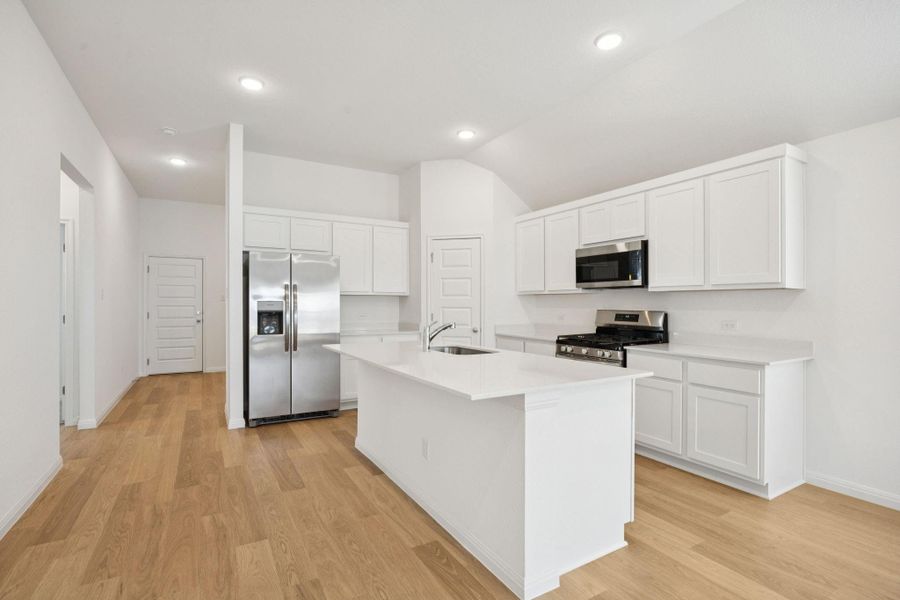 Kitchen featuring stainless steel appliances, white cabinetry, an island with sink, light countertops, and light wood-type flooring