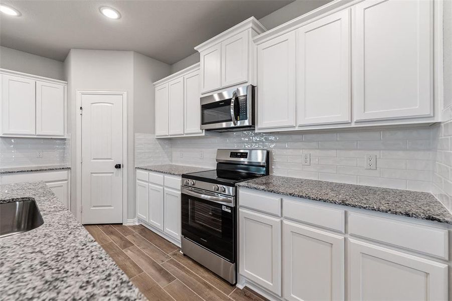 Kitchen featuring stainless steel appliances, white cabinetry, light stone counters, wood finish floors, and decorative backsplash Kitchen featuring stainless steel appliances, white cabinetry, light stone counters, wood finish floors, and decorative backsplash