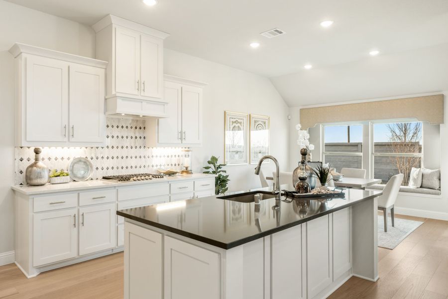 Kitchen with white cabinets, dark granite island, patterned tile backsplash, and hardwood floors open to dining area.