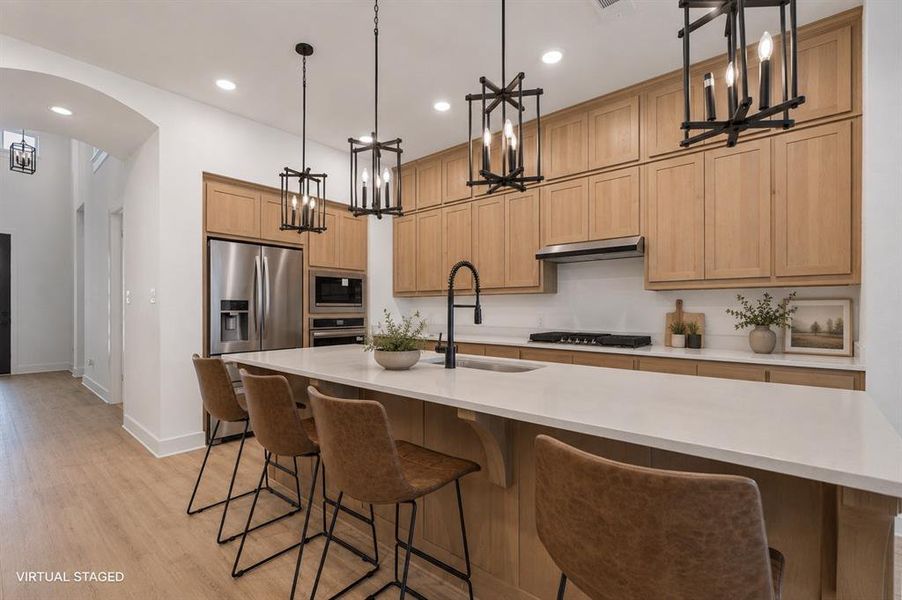 Modern kitchen featuring light wood-finish cabinetry, stainless steel appliances, a white countertop island with seating, pendant lighting, and wood-finish flooring Modern kitchen featuring light wood-finish cabinetry, stainless steel appliances, a white countertop island with seating, pendant lighting, and wood-finish flooring