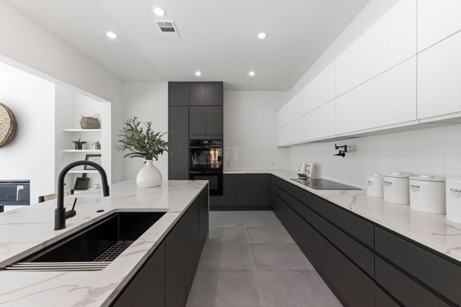 Two tone kitchen with modern cabinets, light stone counters, black appliances, recessed lighting, and two tone cabinetry