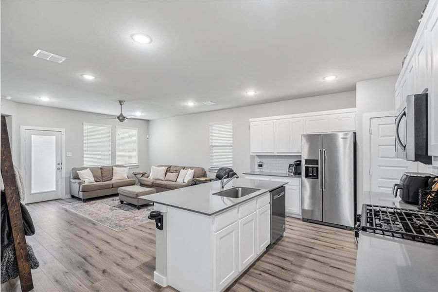 Kitchen with stainless steel appliances, light hardwood / wood-style flooring, a center island with sink, and white cabinetry