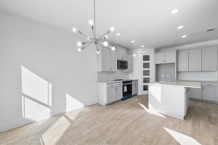 Kitchen with electric range, a notable chandelier, light hardwood / wood-style flooring, a kitchen island with sink, and light stone countertops