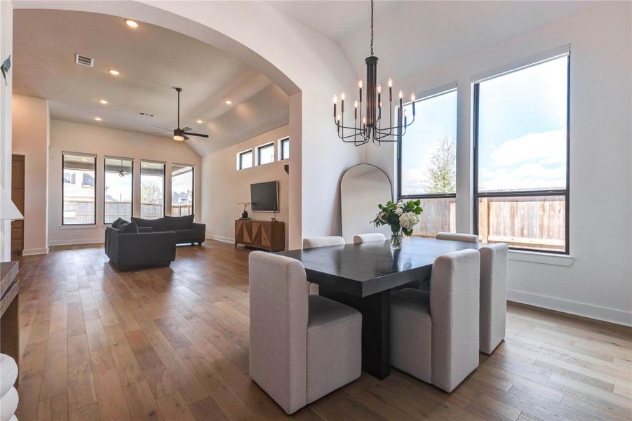 Bright, open-concept living and dining area with high ceilings and large windows for natural light. The space features elegant wood flooring, a modern chandelier above the dining table, and a ceiling fan in the living area, creating a welcoming and spacious atmosphere. Bright, open-concept living and dining area with high ceilings and large windows for natural light. The space features elegant wood flooring, a modern chandelier above the dining table, and a ceiling fan in the living area, creating a welcoming and spacious atmosphere.