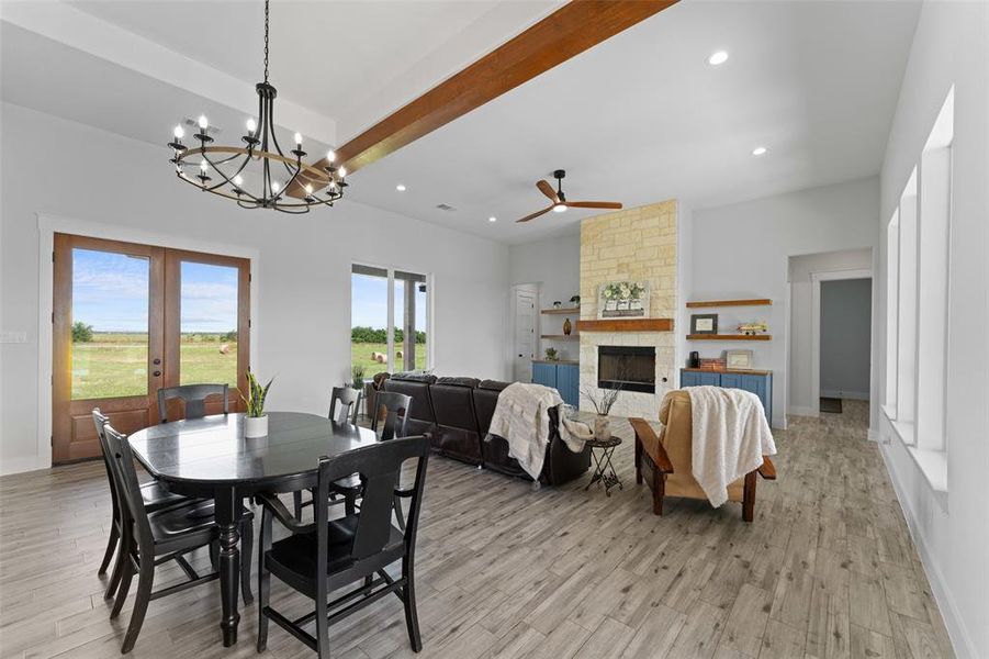 Spacious living area featuring wood-finish flooring, a stone fireplace with a wood mantle, and exposed ceiling beams