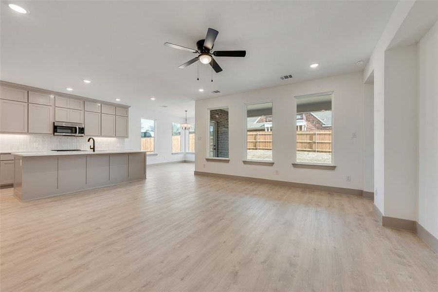 Unfurnished living room featuring sink, ceiling fan with notable chandelier, and light wood-type flooring