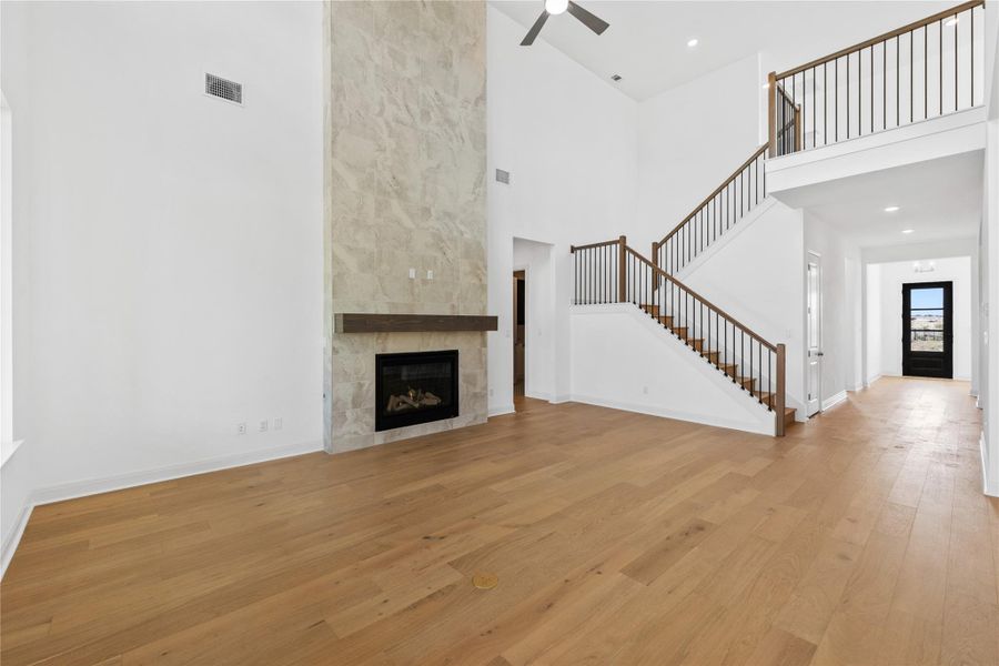 Unfurnished living room featuring a fireplace, light wood-style floors, ceiling fan, a high ceiling, and recessed lighting