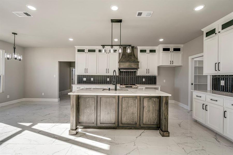 Kitchen with tasteful backsplash, visible vents, marble finish floor, and premium range hood