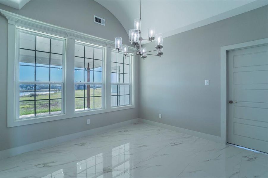 Unfurnished dining area featuring a chandelier, light marble finish floors, and vaulted ceiling