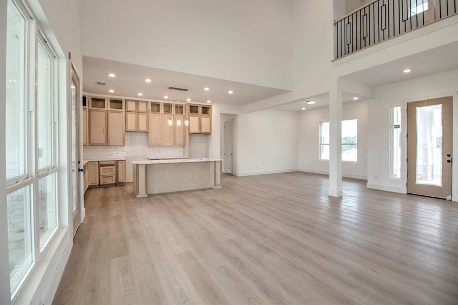 Unfurnished living room with light wood-type flooring, recessed lighting, and a towering ceiling Unfurnished living room with light wood-type flooring, recessed lighting, and a towering ceiling