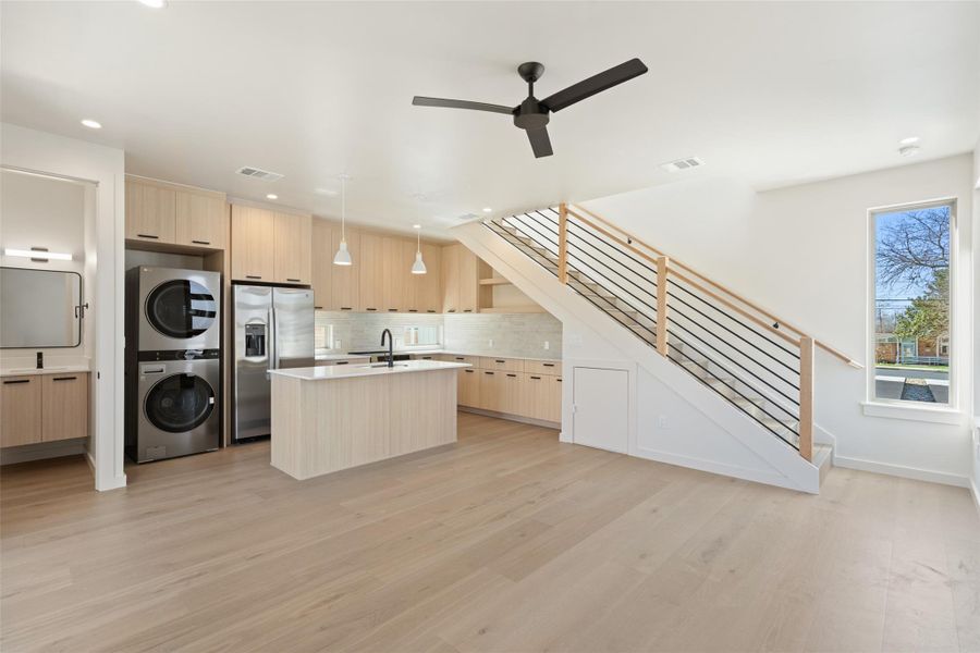 Kitchen featuring modern cabinets, stainless steel refrigerator with ice dispenser, light brown cabinets, and stacked washer / drying machine