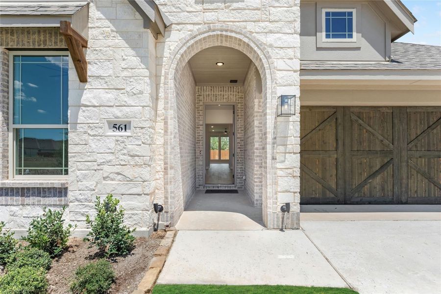 Home entrance with arched brick entryway, stone exterior, and wood garage door beside front door