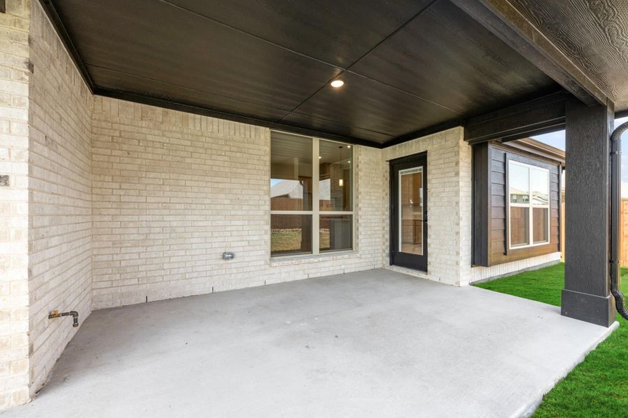 Covered back patio with concrete floor, dark ceiling, brick exterior wall, and glass back door leading inside.