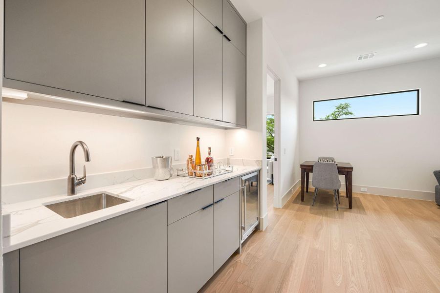[BAR] Perfectly integrated into the game room, the stylish wet bar features a sleek countertop, built-in sink, custom cabinetry, and a beverage refrigerator, making entertaining effortless and elegant.