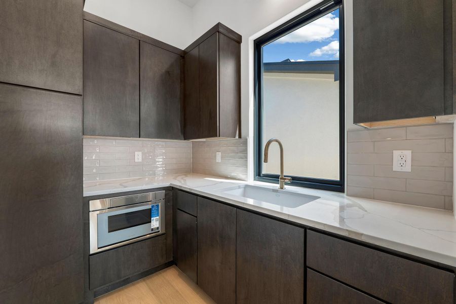 Kitchen featuring dark wood finish cabinets, light stone counters, stainless steel oven, tasteful backsplash, and light wood finished floors