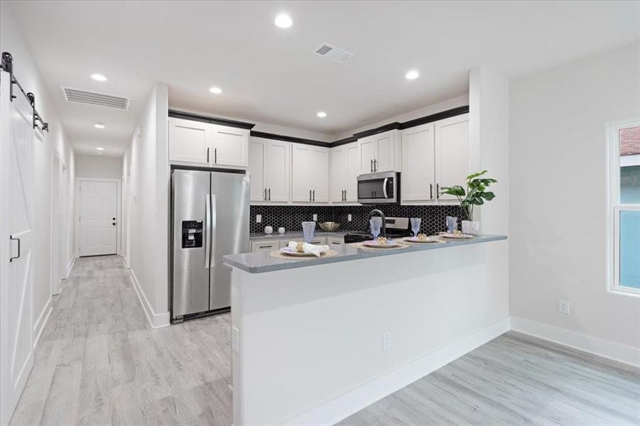 Kitchen with light hardwood / wood-style floors, kitchen peninsula, tasteful backsplash, a barn door, and appliances with stainless steel finishes