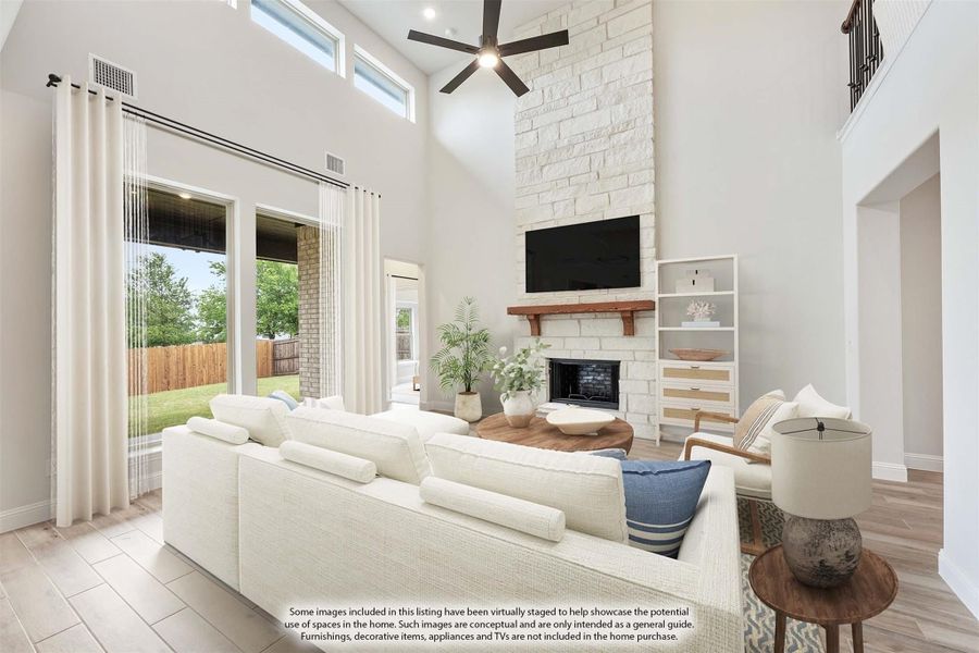 Living room with two-story ceiling, stone fireplace, ceiling fan, and large windows overlooking backyard