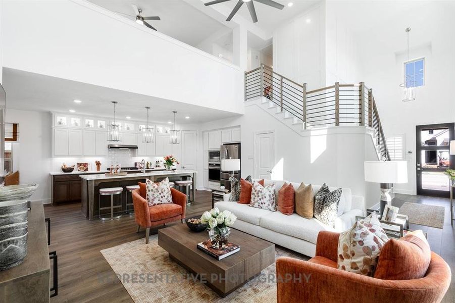 Living room featuring stairway, dark wood-type flooring, a ceiling fan, a high ceiling, and recessed lighting