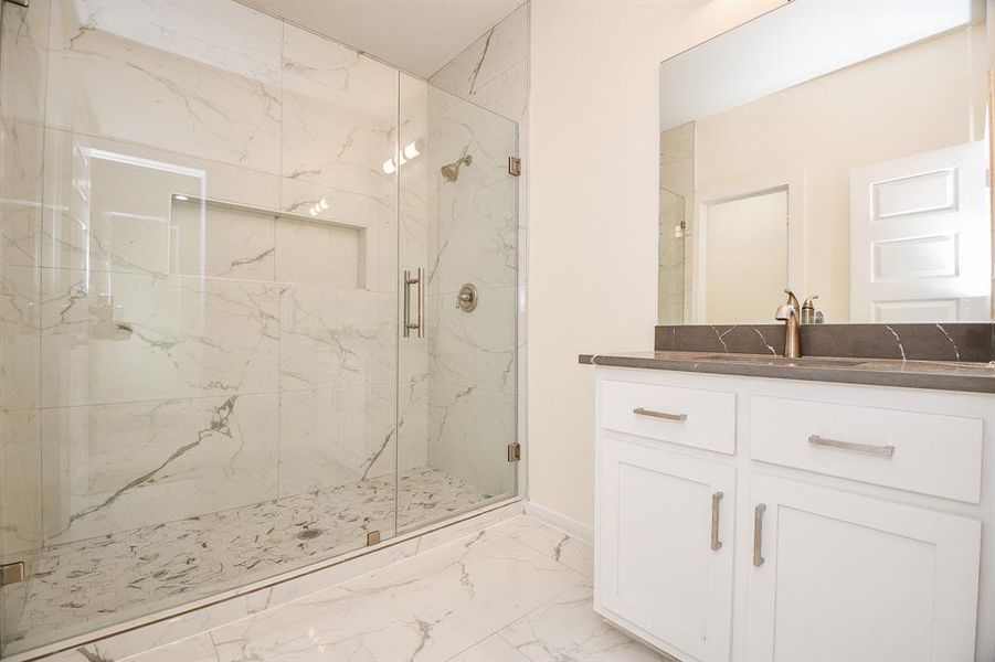 Secondary full bathroom with walk-in shower surrounded by polished porcelain tile walls, single vanity with quartz countertop.