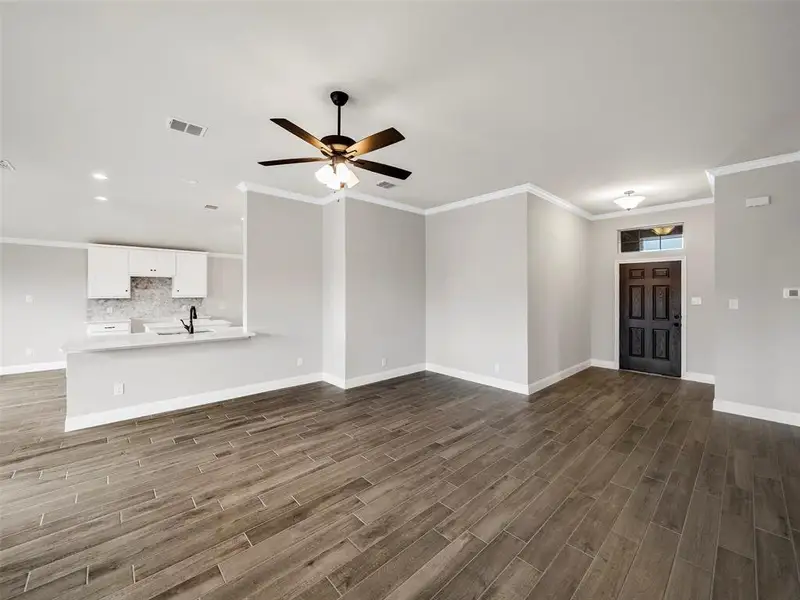 Unfurnished living room with visible vents, baseboards, ceiling fan, and dark wood finished floors