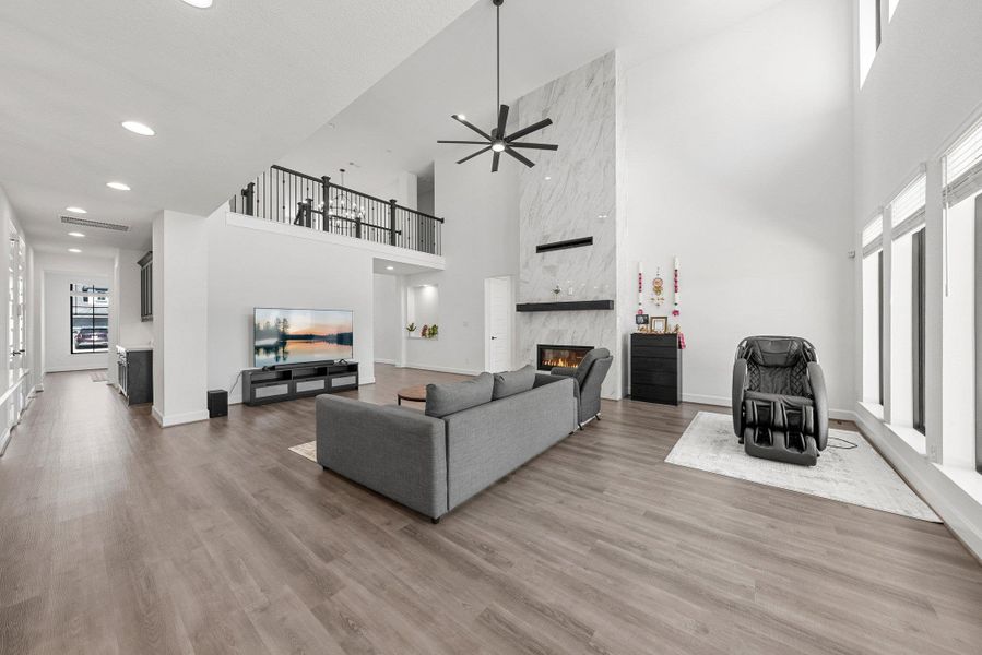 Living room with baseboards, a high end fireplace, wood finished floors, a high ceiling, and recessed lighting