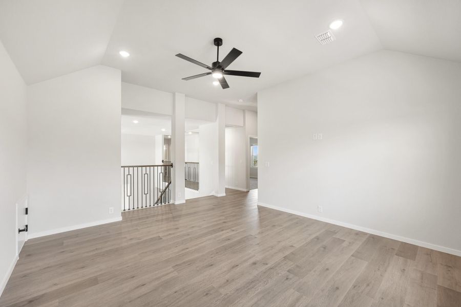 Open living area with vaulted ceiling, black ceiling fan, wood floors, and staircase railing visible in background. Open living area with vaulted ceiling, black ceiling fan, wood floors, and staircase railing visible in background.
