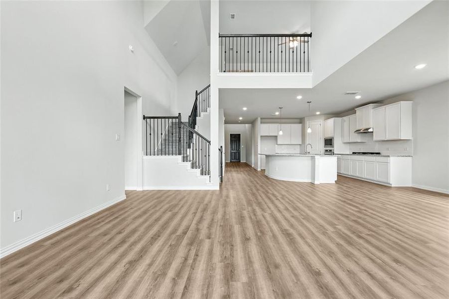 Unfurnished living room featuring a high ceiling, light wood finished floors, stairway, and recessed lighting Unfurnished living room featuring a high ceiling, light wood finished floors, stairway, and recessed lighting